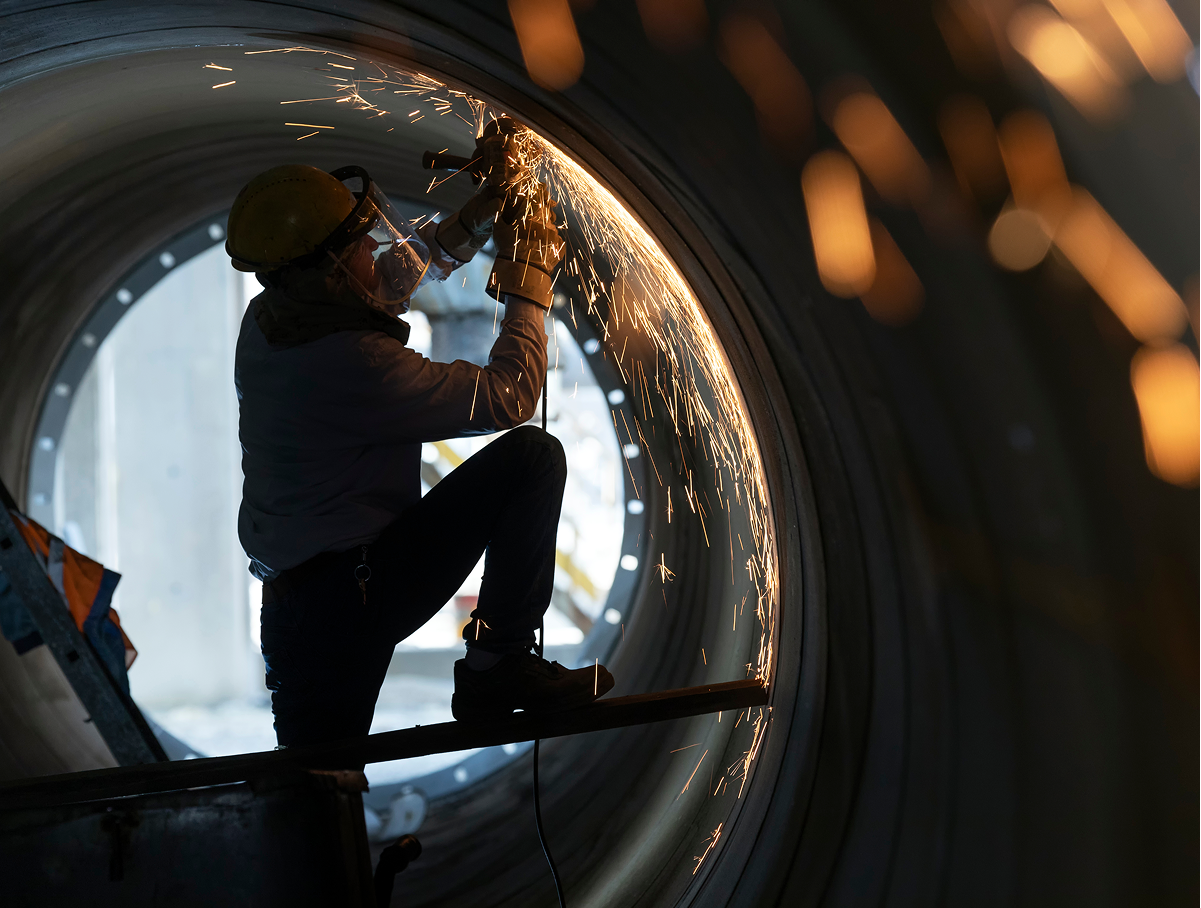 A person welding in a cylindrical metal structure.