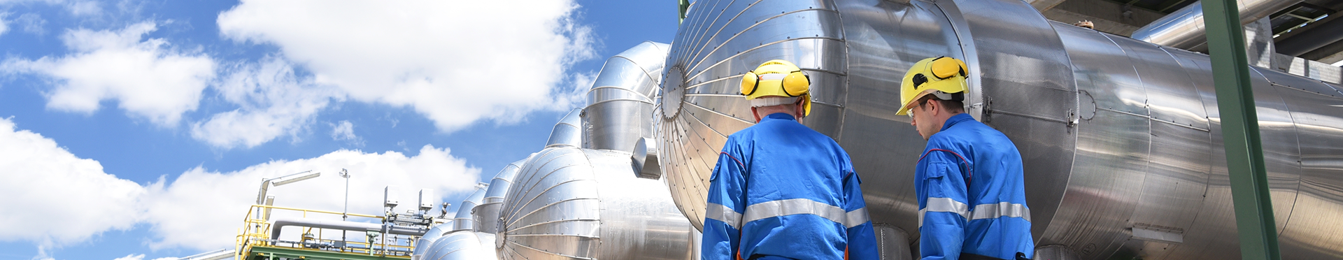 Two men in hard hats inspect a large metal cylinder on an industrial site